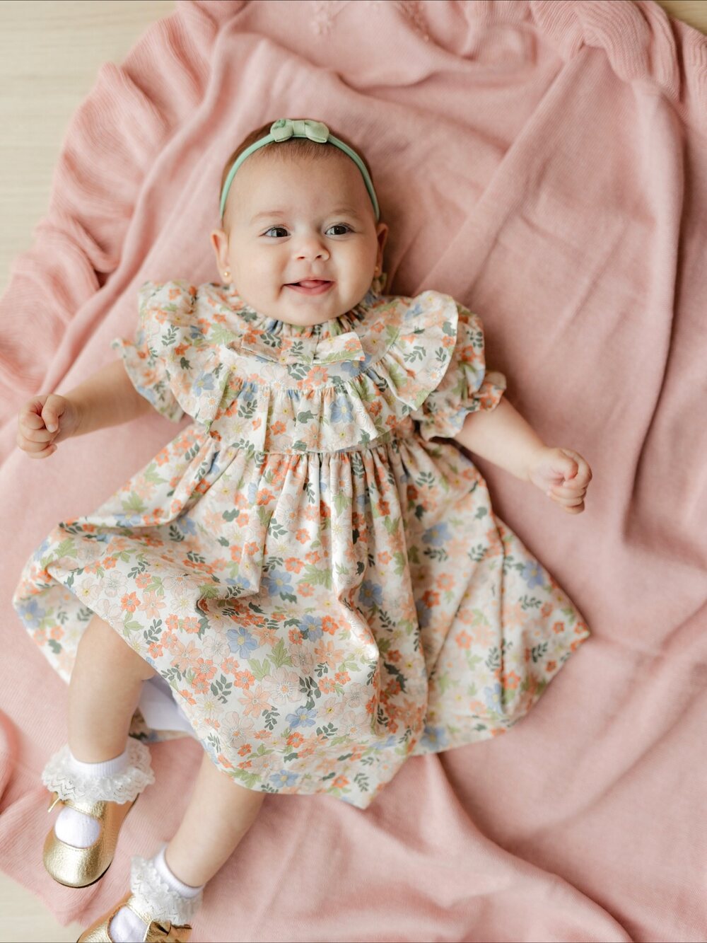 Bebê de vestido florido deitada sobre manta rosa
