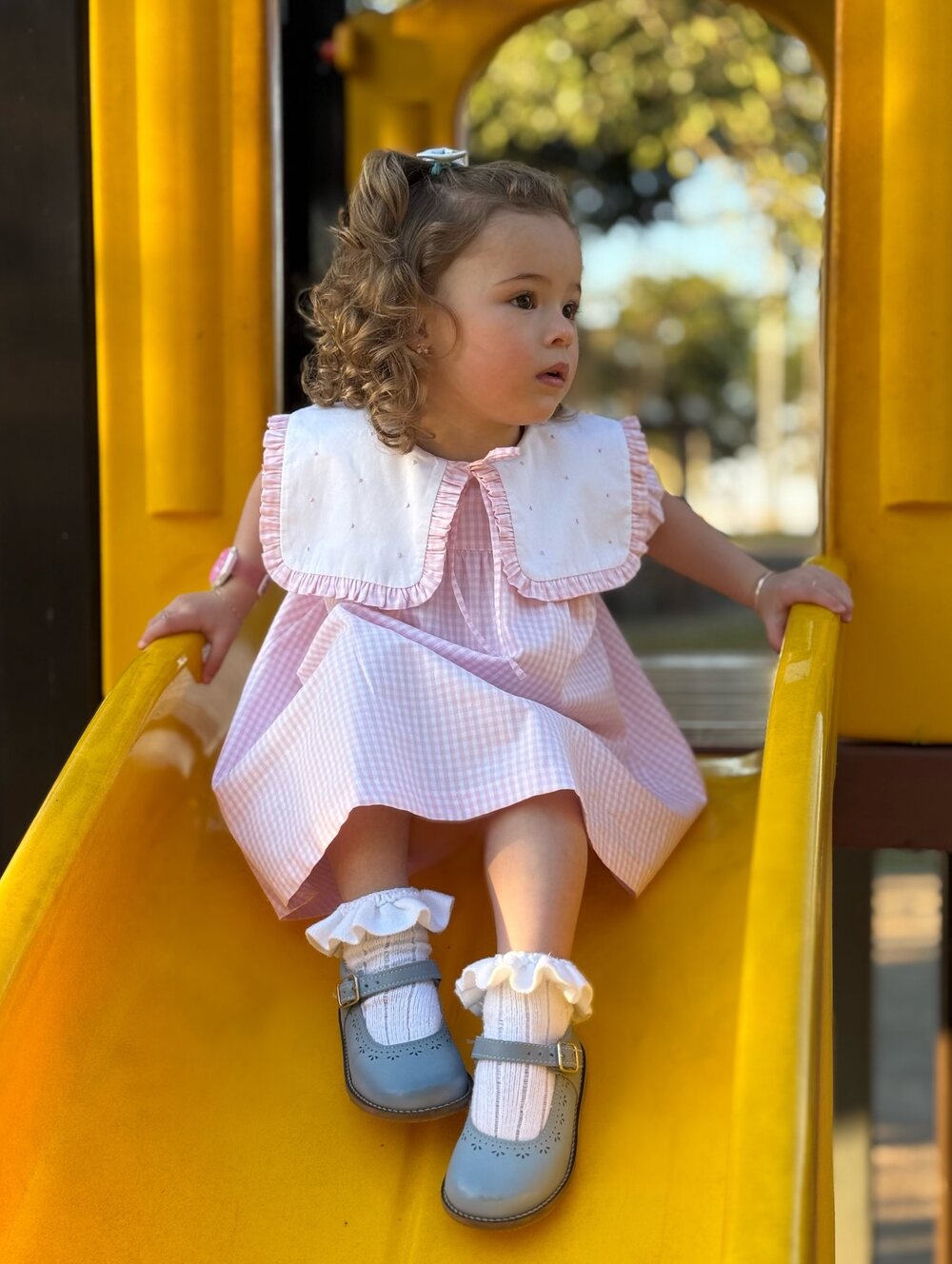 Menina de vestido rosa com gola bordada brincando no escorregador
